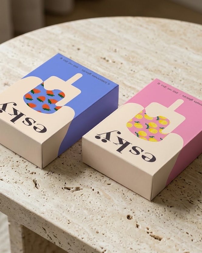 Deux boîtes de bâtonnets glacés esky, fraise sur fond bleu et citron sur fond rose, posées sur une table en travertin