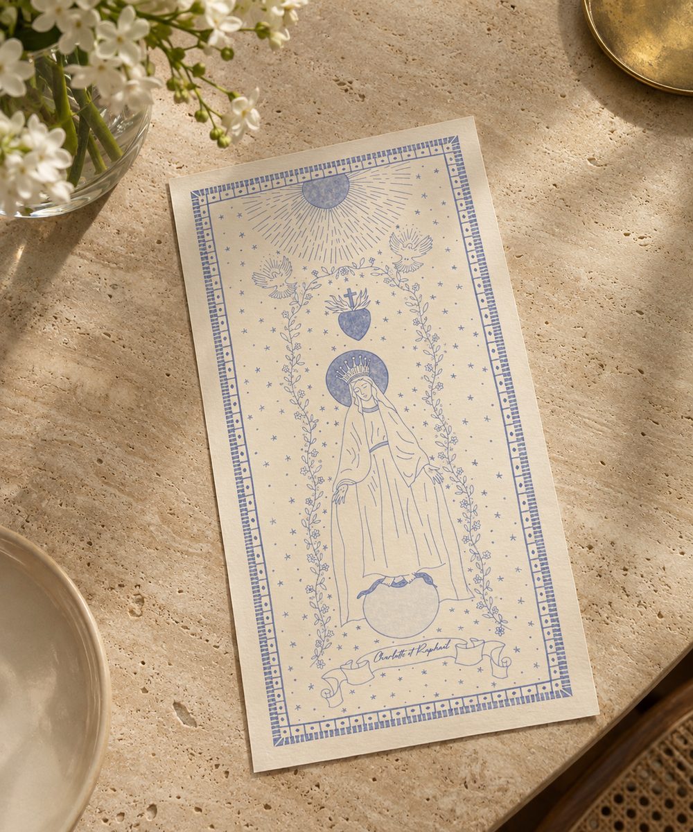 Image pieuse illustrée de la Vierge Marie au trait bleu, posée sur une table en travertin près d’un bouquet de fleurs blanches