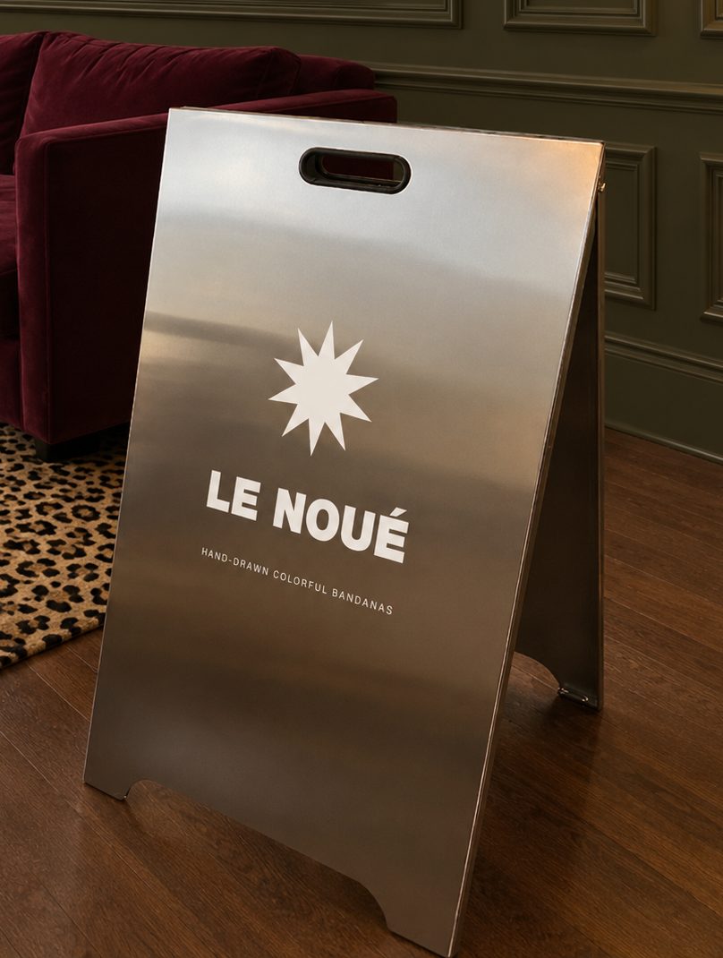 Chevalet en inox Le Noué, étoile et logo blancs, dans un salon au parquet foncé